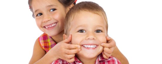 Two funny smiling little children, showing their teeth, isolated on white